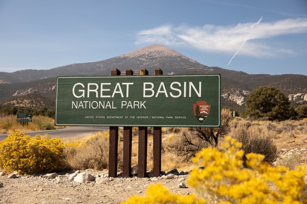Entrance to the Great Basin National Park with the sign in full view of the reader and yellow shrubbery on the right