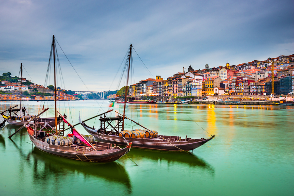 Two traditional Rabelo boats that carry wine barrels docked in the harbor at dusk on a nice day to show the best time to visit Porto