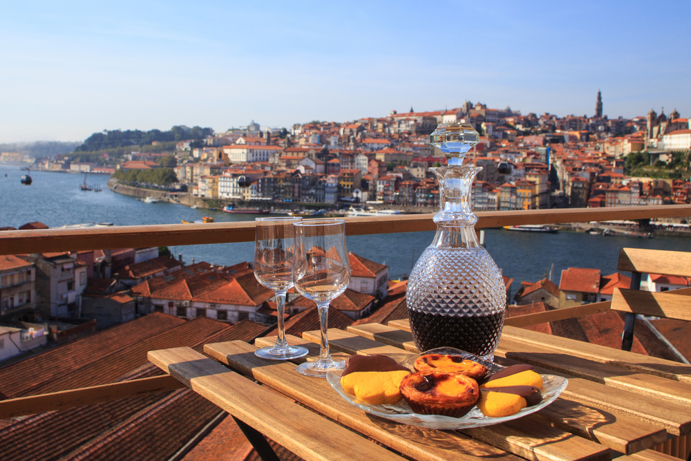 Concept of outdoor dining with Port wine in a decanter with glasses and snacks as the table overlooks the river and houses across it for a frequently asked questions section in a piece about the best time to visit Porto