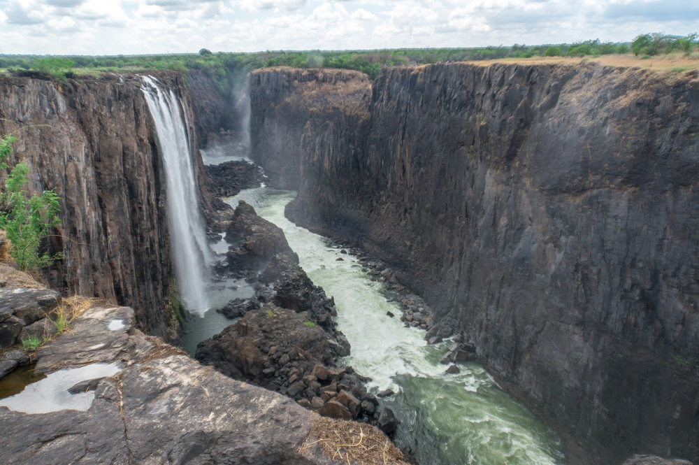 Gorgeous view of the narrow rock face into which Victoria Falls pours with a cloudy sky overhead
