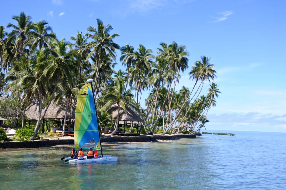 Tropical island of Vanua Levu, one of the best areas in Fiji, pictured with a colorful sailboat on the water just off the coast