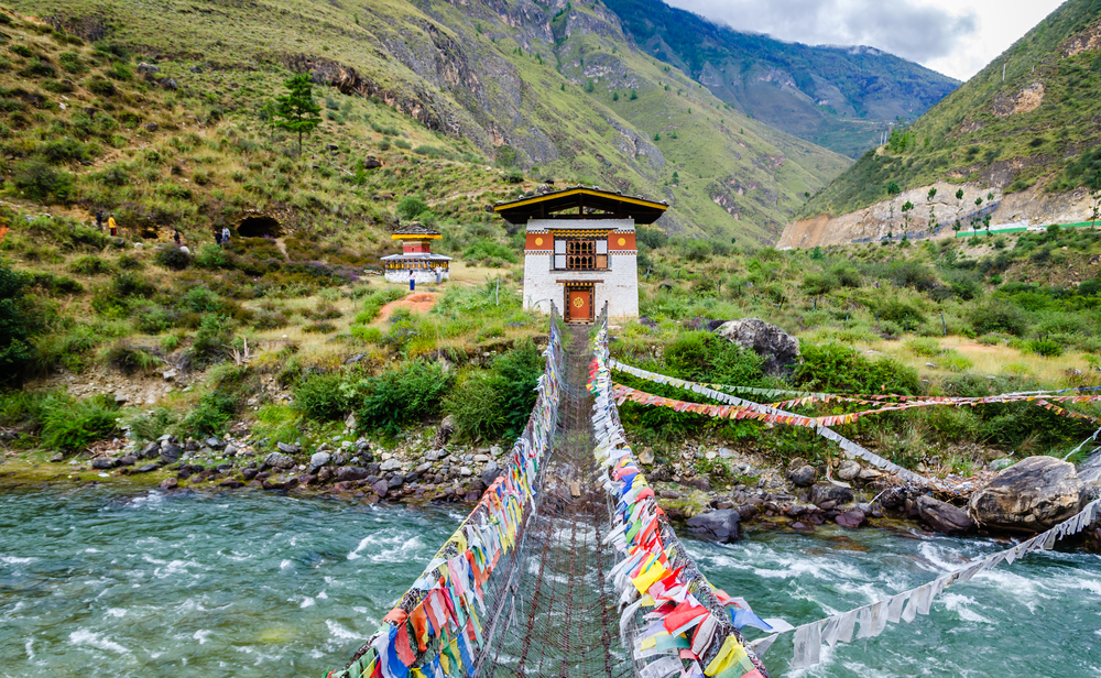 Iron chain bridge leading to the Tamchog Lhakhang Monastery with a river rushing below and prayer flags on the iron wire