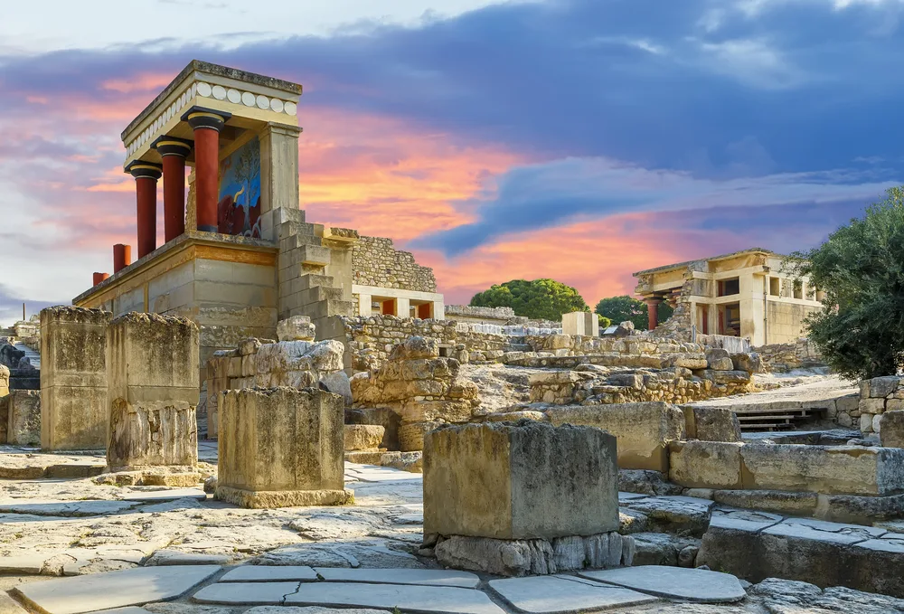 Picturesque view of the old ruins of the Knossos Palace in Crete pictured during the best time to visit with a pink and orange dusk sky overhead