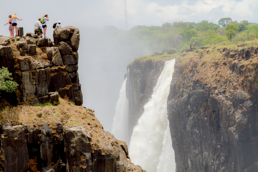 A group of young women in blue and black shirts overlooking the waterfall for a piece titled Is Victoria Falls Safe to Visit