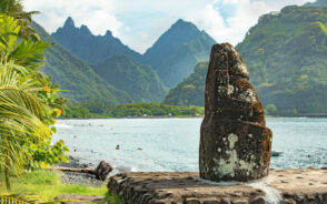 Neat view of a stone monument in Tahiti with a giant mountain and bay behind it for a piece titled Is French Polynesia Safe to Visit