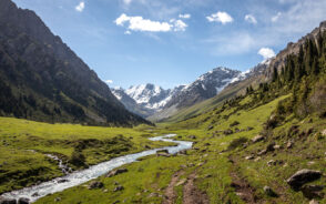 Featured image for a guide titled Is Kyrgyzstan safe to visit featuring a giant mountain range with a stream running down the middle