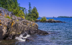 Coastline of the Isle Royale National Park in Michigan pictured on a clear day with the clear and cold water lapping the rocky shoreline