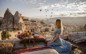 Woman sitting on a rooftop in a blue sundress looking at the hot air balloons in Cappadocia to show that it is very safe to visit