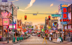 Photo of the popular Beale Street area with lots of little shops surrounding the brick road with neon signs advertising clubs wherever the eye can see for a piece titled Where to Stay in Memphis