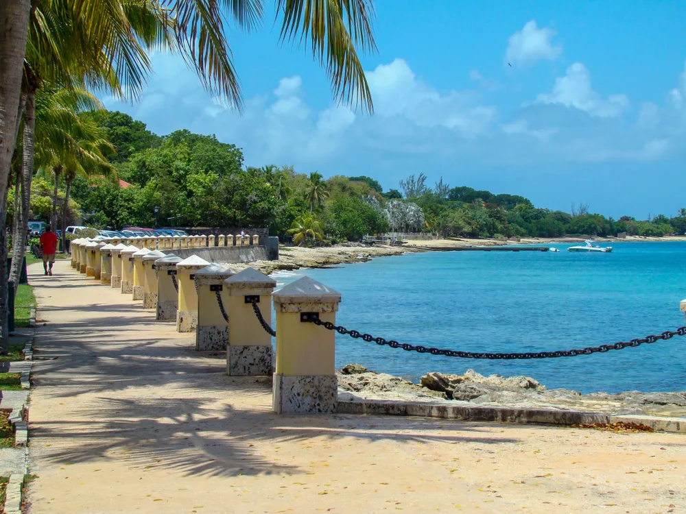 Frederiksted foreshore sidewalk next to the blue water for a piece titled Is St. Croix Safe to Visit and palm trees on the right side of the path
