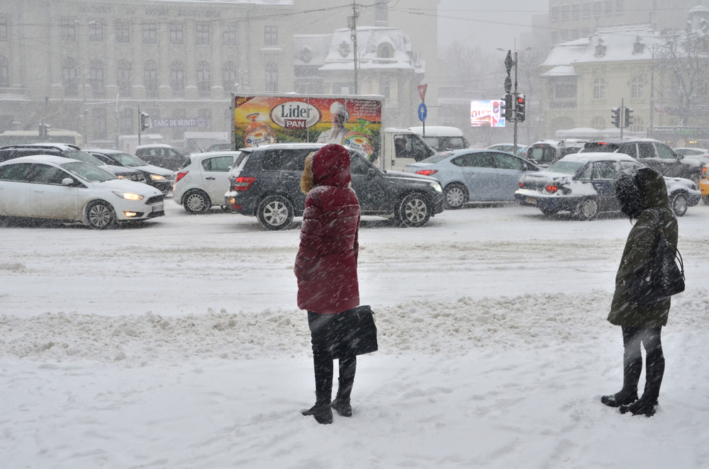 Woman in a parka standing outside of a building waiting for a taxi in the middle of winter in Bucharest during the worst time to visit Romania