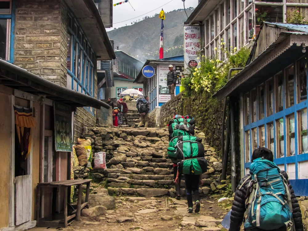 Photo of people walking along the street in Phakding and carrying bags to help answer the question is Nepal Safe to Visit