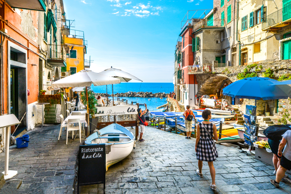 Two women walking along the street by a cafe in the small Italian town of Riomaggiore as an image for a guide to whether or not Cinque Terre is safe to visit