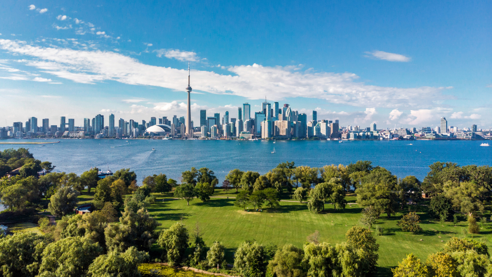 Toronto skyline shown with Lake Ontario and a green park in the foreground to show which cities are the 10 cheap places to fly to