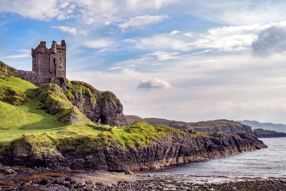 View of an old castle ruin in the Scottish highlands on a nice spring day with green grass and rocky coasts to show why you should visit Scotland