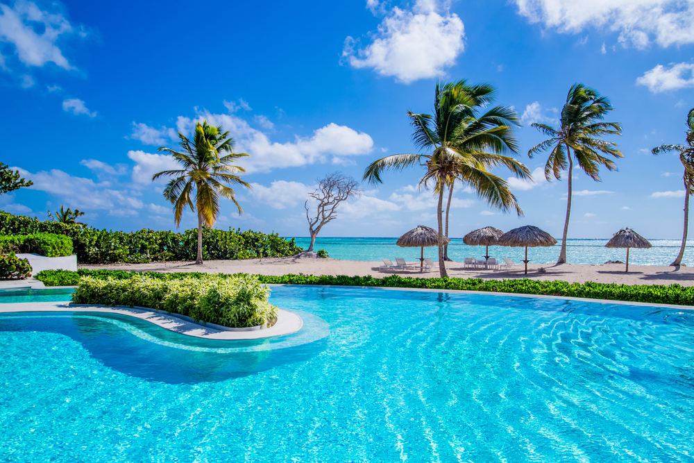 Infinity swimming pool directly in front of the Caribbean Sea with palm trees, greenery, and umbrellas on the beach to show what's at the best adults only all inclusive Caribbean resort properties