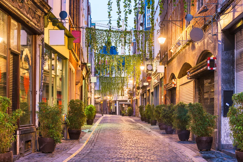 Evening view of a quaint cobbelstone street in Brussels pictured with shops on either side and lights illuminating the outside of the buildings