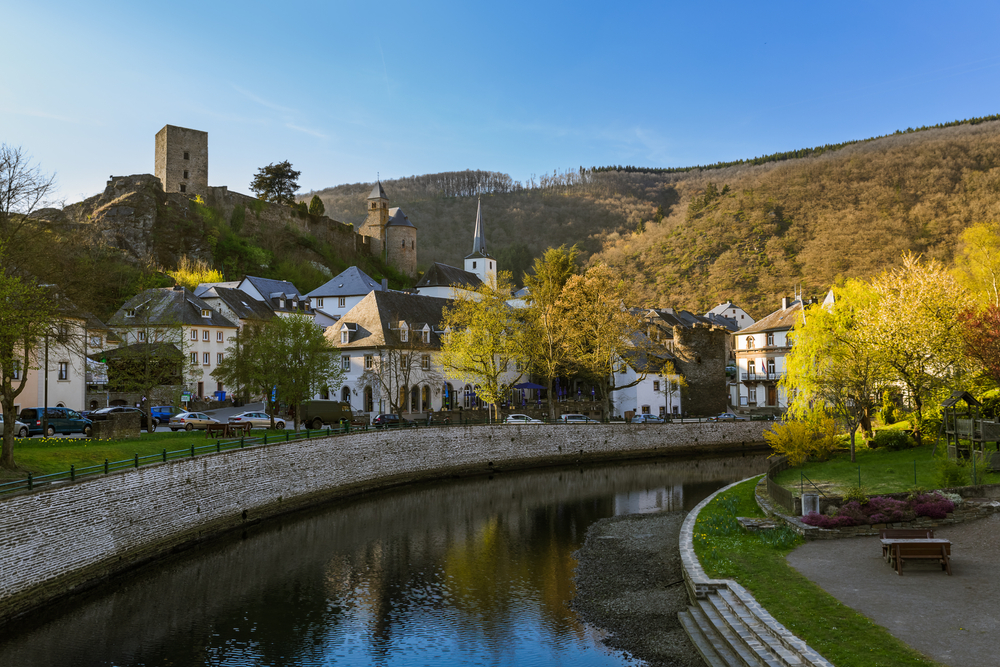 Village Esch pictured during the best time to visit Luxembourg with a river running through the old-style homes pictured on a clear-sky day