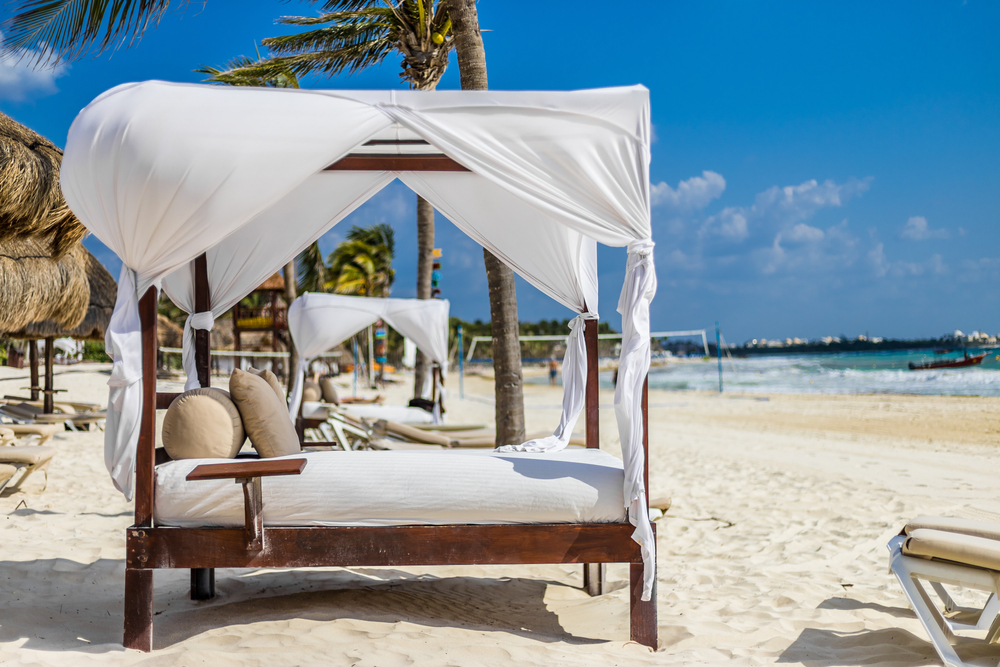 Pictured luxury beach cabana on the sand in Cancun is like those offered at the best adults-only all-inclusive resorts in Cancun with a shade canopy and comfortable lounge chair