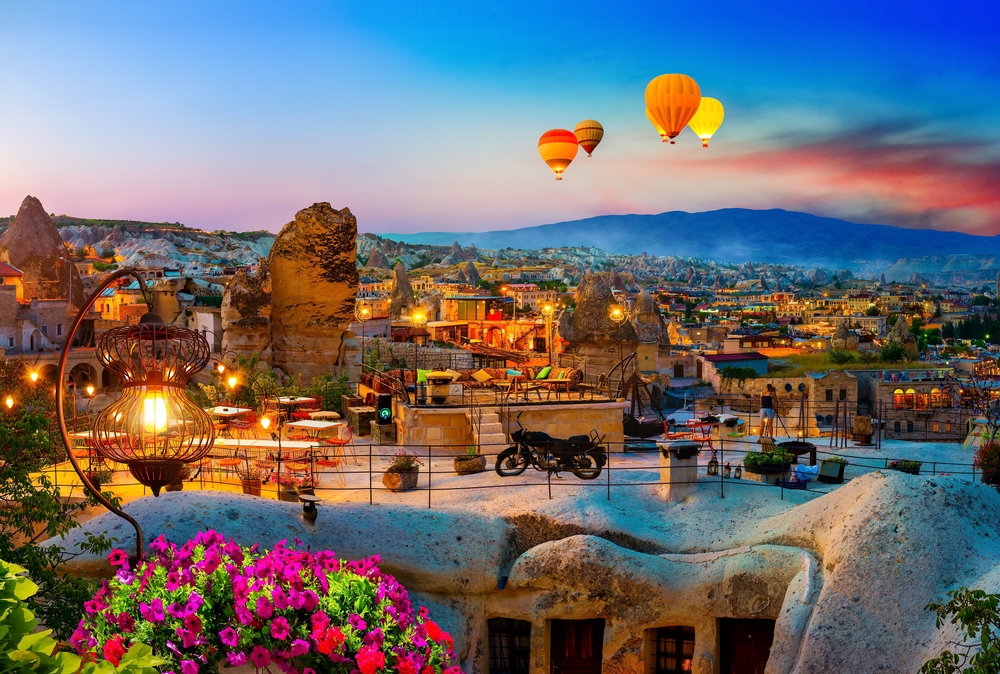 Goreme town in Cappadocia pictured with hot air balloons illuminated at night and a motorcycle on a stone house