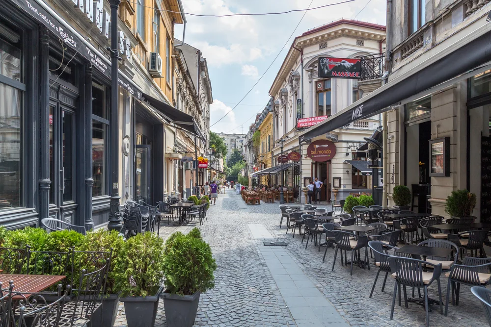 Narrow alleyway pictured in Bucharest with cloudy skies overhead and empty chairs outside of the restaurants, seen during the best time to visit Romania