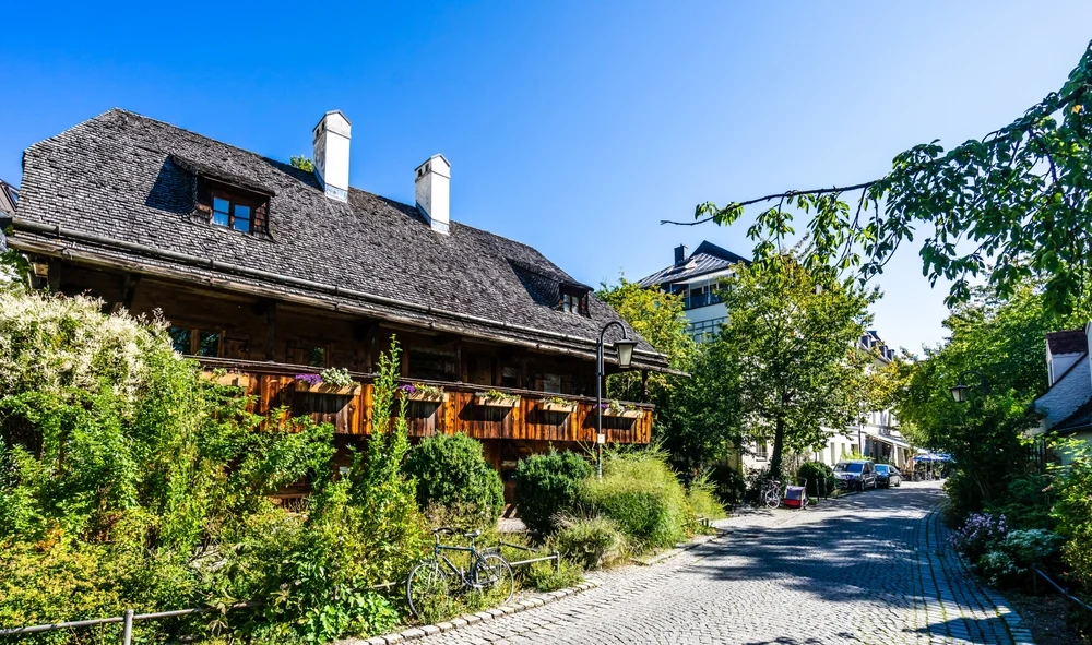 Au-Haidhausen, one of the most peaceful areas in Munich, pictured as a featured place to stay, seen with its picturesque cobblestone streets and wooden homes with shrubbery covering them and bikes scattered about