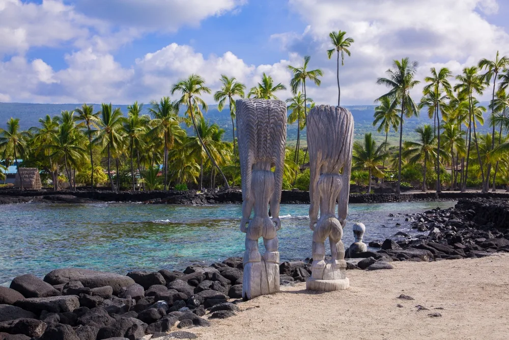 Unique view of tiki heads in front of black volcanic rock at a historical park in Kona for a piece on whether or not the island is safe to visit