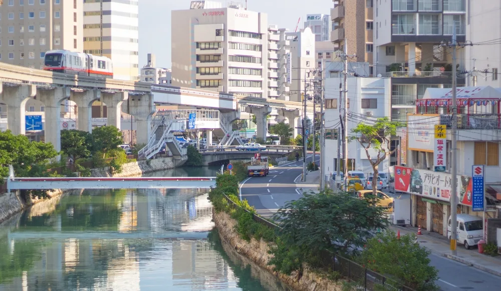 Calm morning during the overall best time to travel to Okinawa with an elevated monorail making its way down the tracks above the street between modern apartment buildings