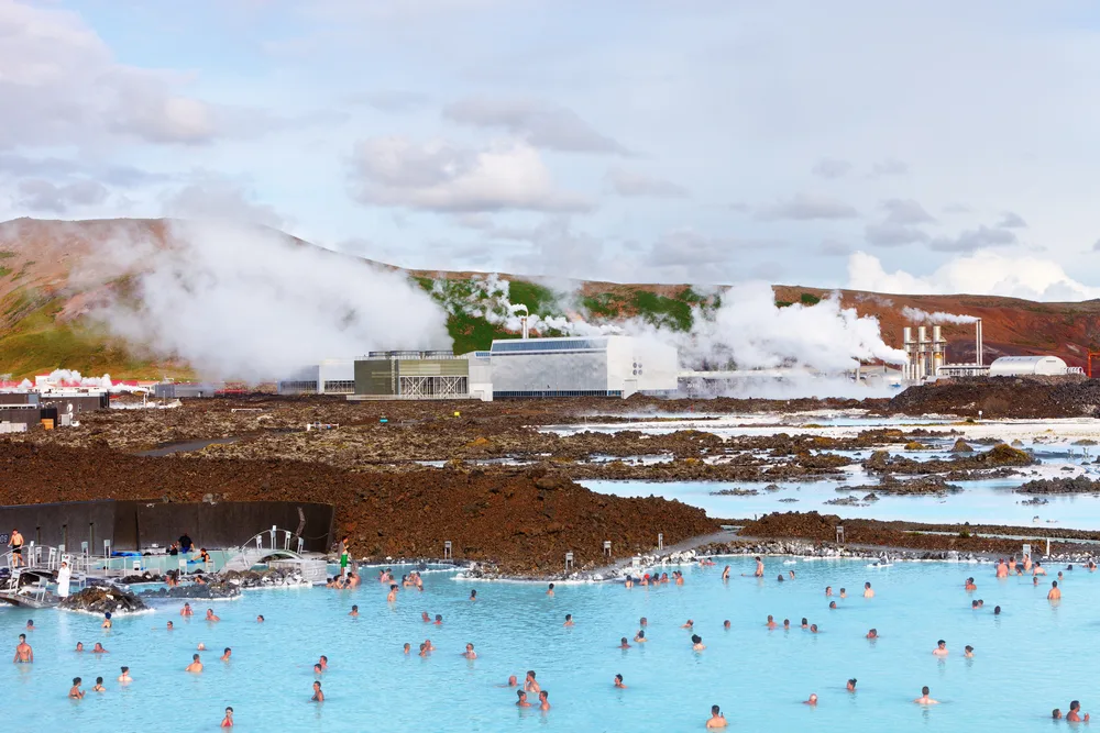 For a guide to whether it's safe to visit the Blue Lagoon, pictured are countless people in the neon-teal water with a power station in the background