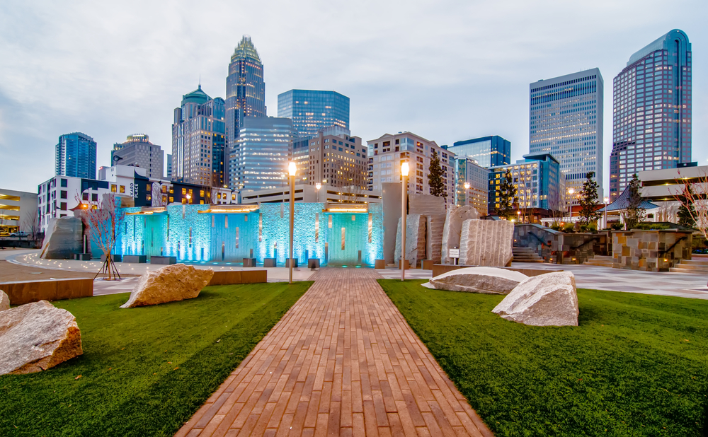 Charlotte, North Carolina downtown skyline shown on a cloudy day with a wooden path leading to an exhibit to shown an example of the cheapest places to fly