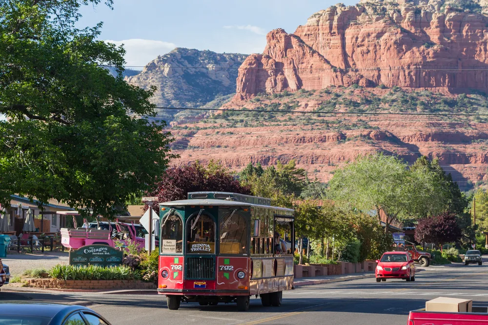 View of the Sedona Trolley shuttling tourists around the city with red rocks looming in the background for a frequently asked questions section covering the best boutique hotels in Sedona