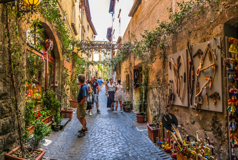 Tourists in a neat corridor of Florence with vine-lined brown and orange walls and a stone walking path