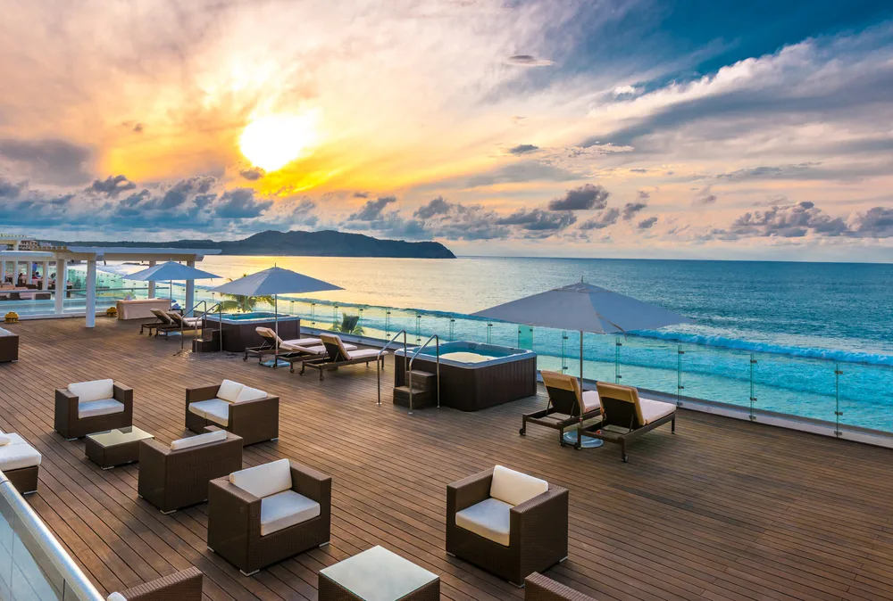 Caribbean beachfront dining at one of the best adults only all inclusive Caribbean resort restaurants at sunset with tables, chairs, and umbrellas overlooking the ocean