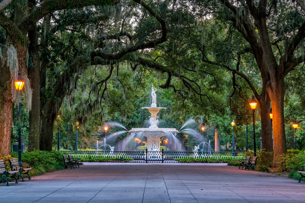 Magnificent white fountain pictured in the middle of Forsyth park with a tree-lined walkway leading to the fountain
