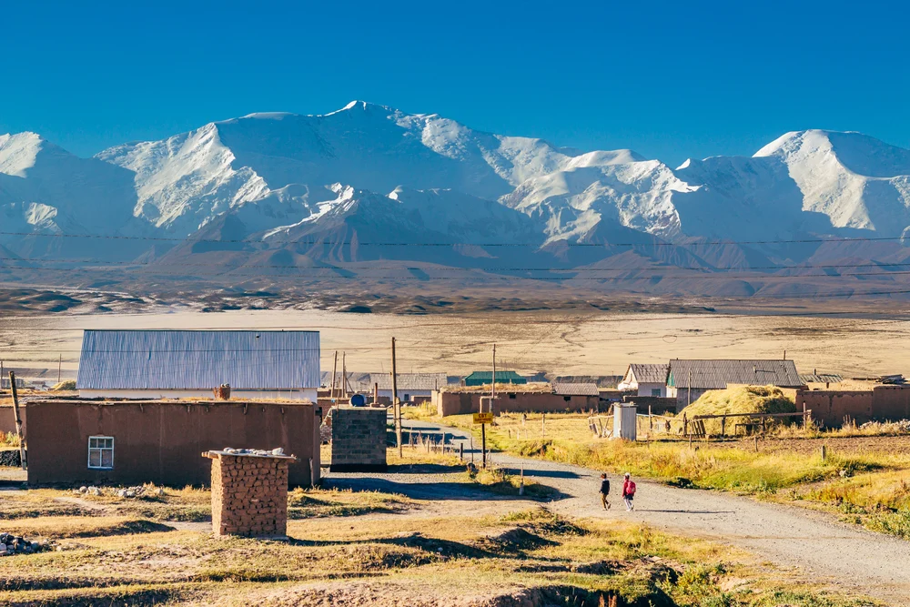 Small village in the town of Sary-Mogul with a few tin-roofed buildings in the middle of a wheat field in the Pamir mountains for a piece on whether or not Kyrgyzstan is safe to visit