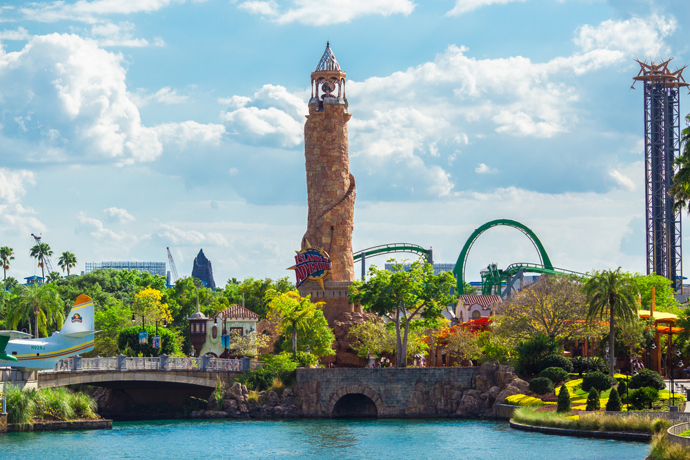 Universal Studios entrance to Islands of Adventure with a lighthouse and roller coasters on a nice day during the summer as one of the best US spots for a vacation
