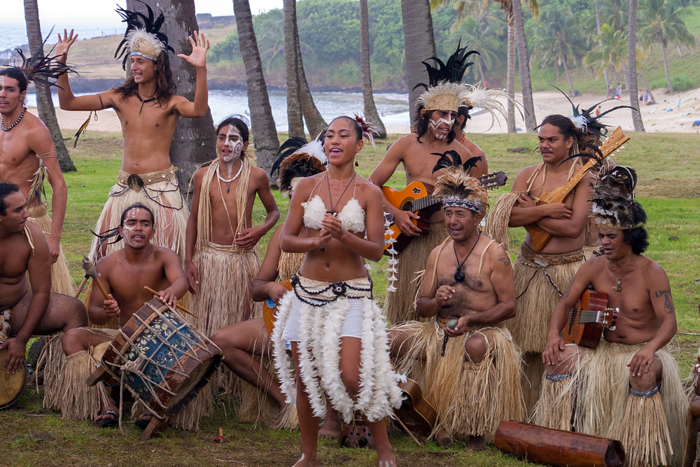 Locals performing a traditional polynesian dance during the best time to go to Easter Island while wearing white bikini tops and grass skirts