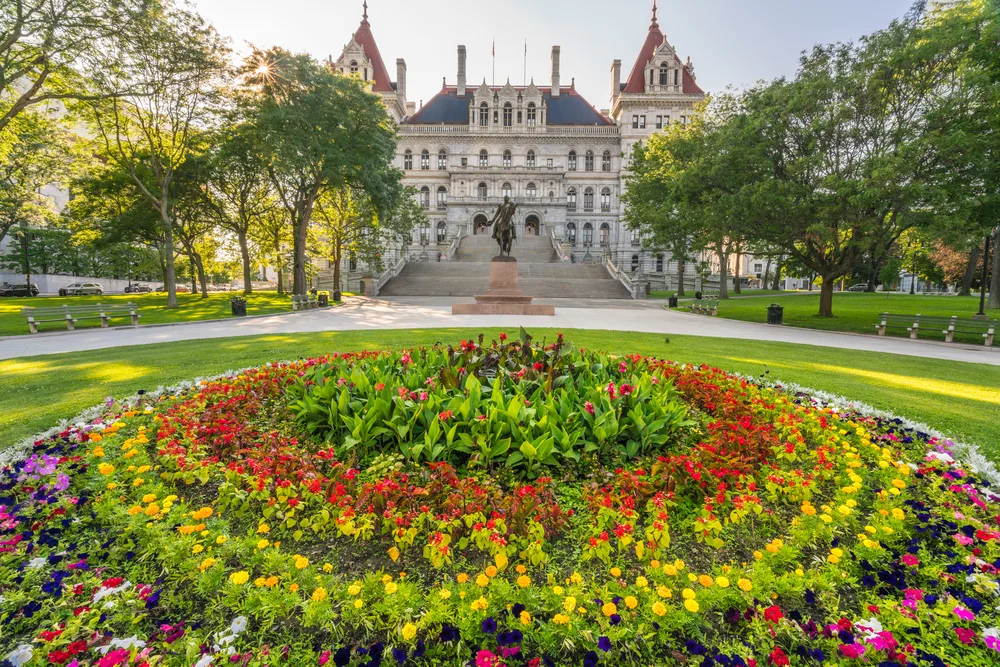 The New York State Capitol Building with flowers in a round bed in front show an example of sights to see in Albany, where flights are cheap
