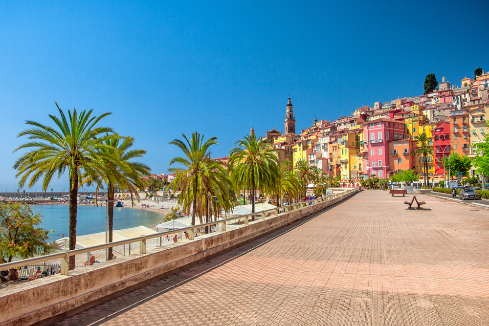 Stone boardwalk running along the crescent-shaped beach under a blue sky for a piece titled Where to Stay in Monaco