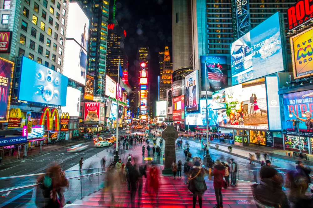 View of Times Square in NYC at night with LED advertisements lighting up the roads as visitors walk around for a piece showing the 10 best US vacations you can take