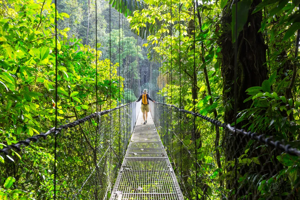 Woman crossing a metal suspension bridge in Costa Rica for a guide to what a trip to the country costs