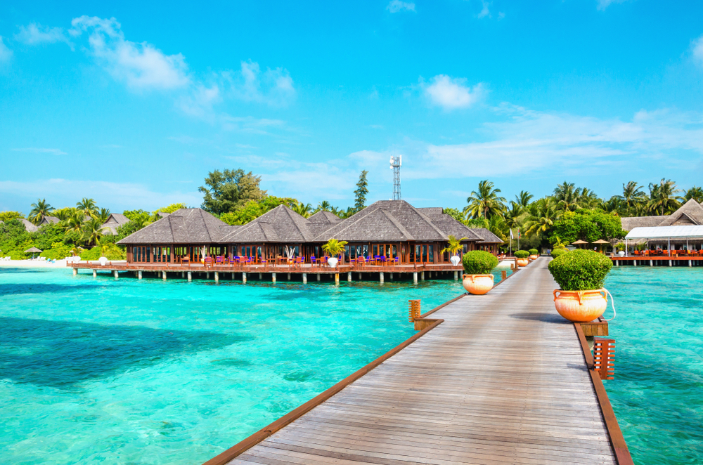 Sandy beach and wooden pier leading to over-water huts in the Maldives for a guide to the average trip costs