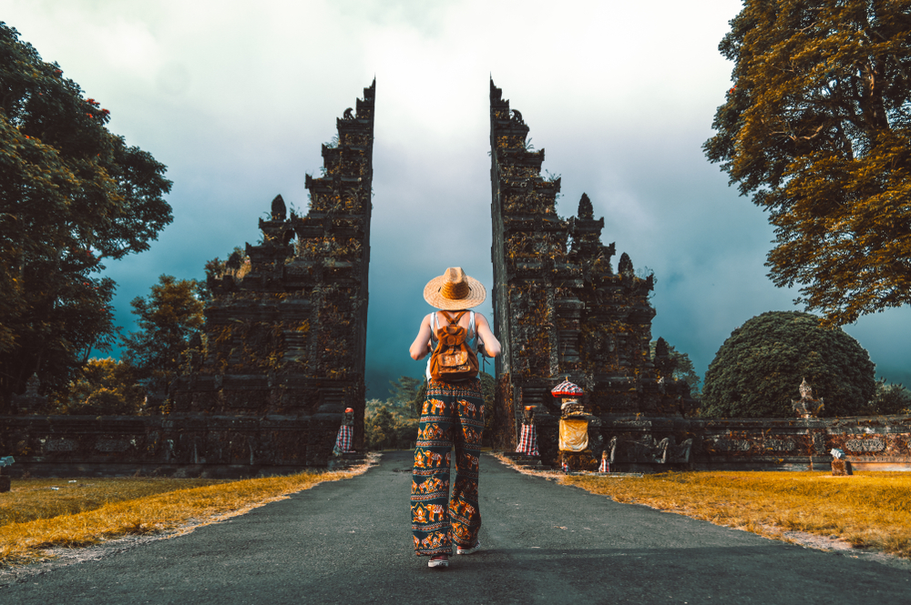 Woman in traditional clothing standing with a backpack outside of temple gates in Bali for a guide to the best time to visit Asia