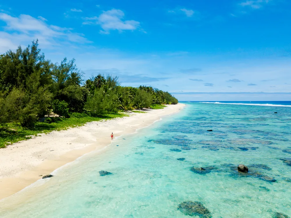 Aerial image of a lone person walking along the white-sand beaches of Titikaveka in Rarotonga, one of the best places to stay in the Cook Islands