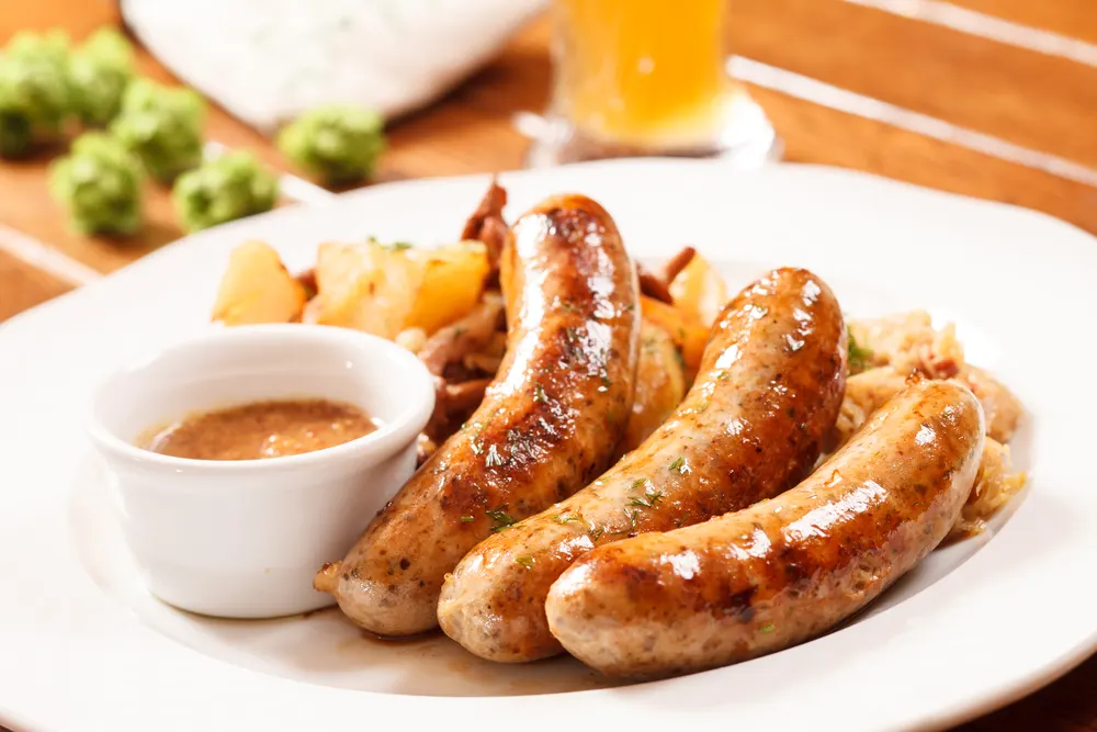 Three German bratwurst links on a plate with cabbage and mustard dipping sauce to show one of the best German foods to try
