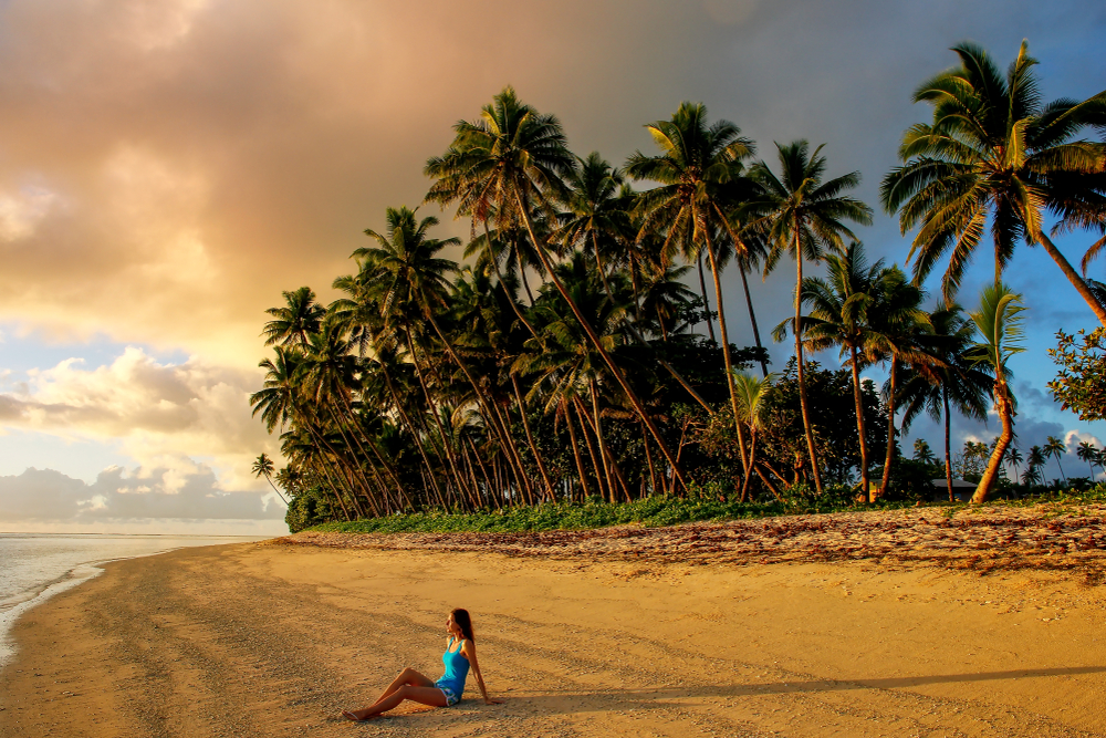 Young woman sitting on the beach at dusk on Taveuni Island in Fiji for a guide to what it costs to go there