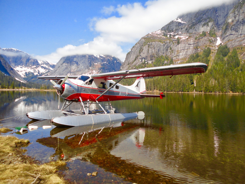 Photo of a red and white floatplane pictured on the water in a valley next to mountains for a guide to the average Alaskan vacation cost