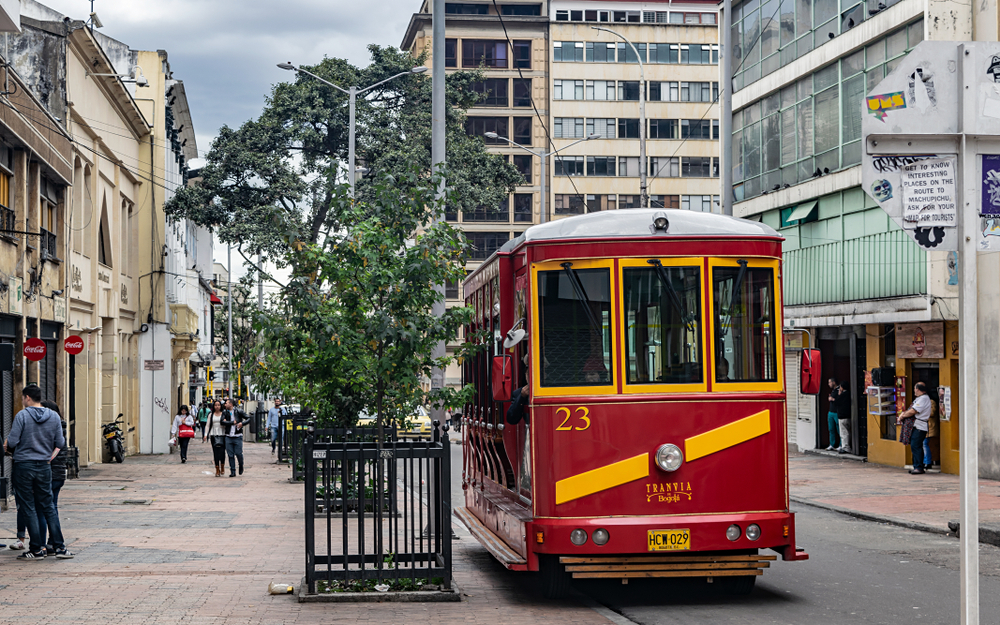 As an image for a guide titled The Best and Worst Times to Visit Bogota, a red trolley sits in the middle of the street in the old part of town