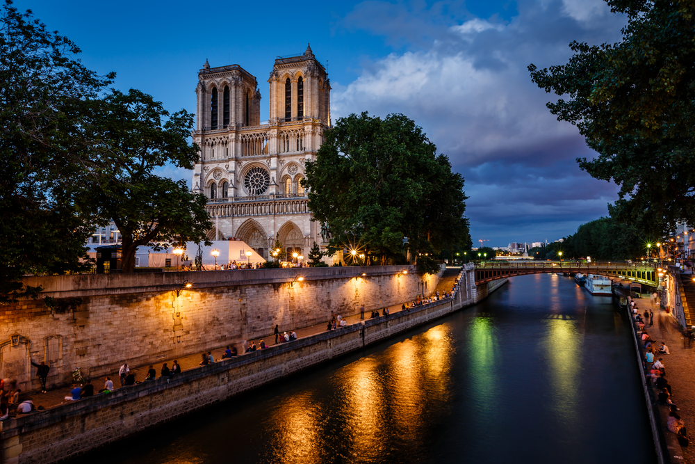 Notre Dame cathedral pictured at night with a picturesque cloudy and moonlit sky above the trees