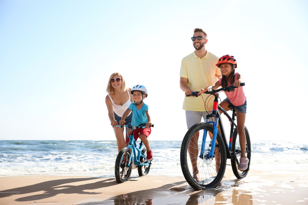 Parents help their children ride bikes along the shore while enjoying one of the best spring break vacations as a family